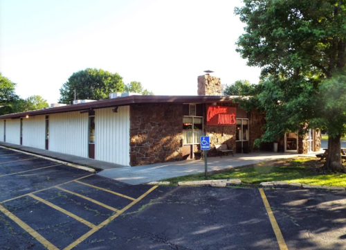 A single-story restaurant with a stone facade and large windows, surrounded by trees and a parking lot.